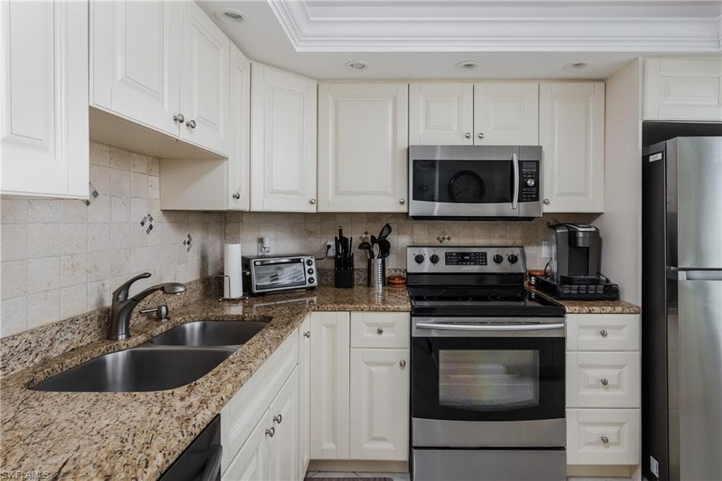 Kitchen featuring light stone countertops, stainless steel appliances, and white cabinetry