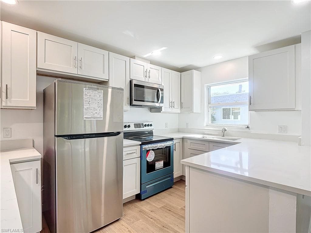 Kitchen with light hardwood / wood-style flooring, white cabinetry, appliances with stainless steel finishes, and sink
