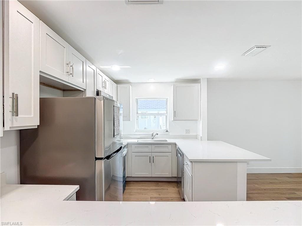 Kitchen featuring stainless steel appliances, white cabinets, kitchen peninsula, and light hardwood / wood-style floors
