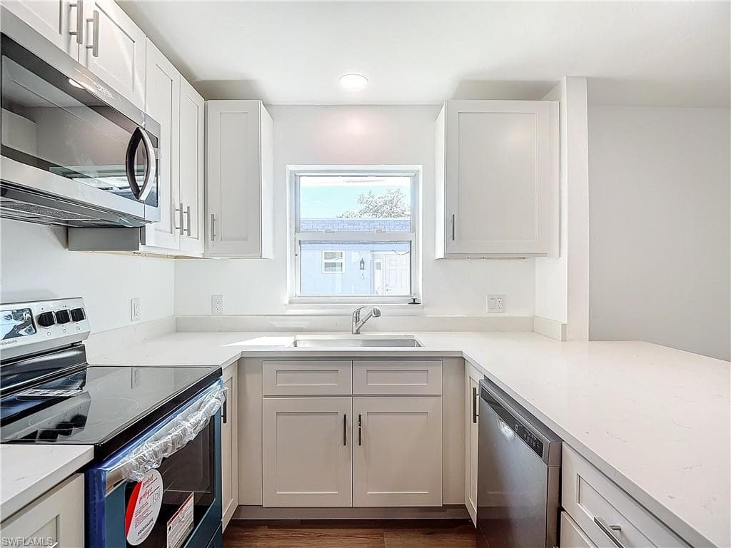 Kitchen with appliances with stainless steel finishes, light stone counters, white cabinets, dark hardwood / wood-style floors, and sink