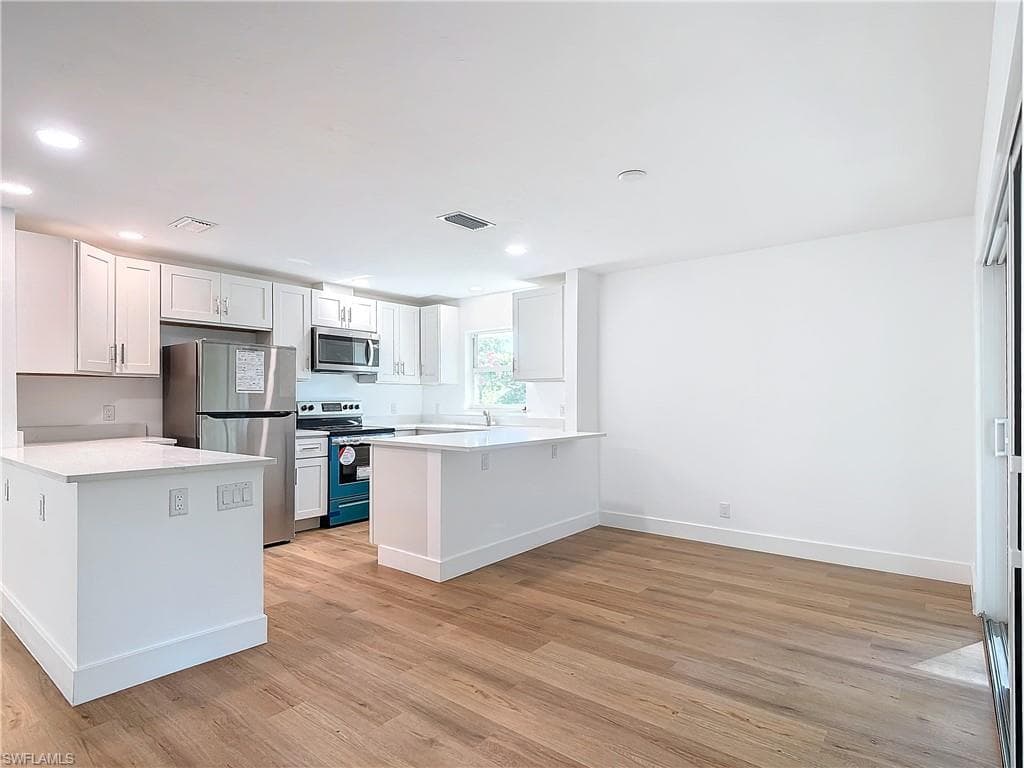 Kitchen with kitchen peninsula, light hardwood / wood-style flooring, white cabinetry, stainless steel appliances, and a kitchen breakfast bar