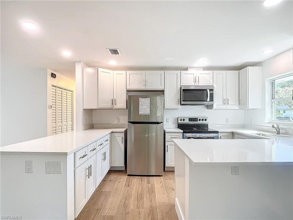 Kitchen featuring kitchen peninsula, light hardwood / wood-style flooring, stainless steel appliances, and white cabinets