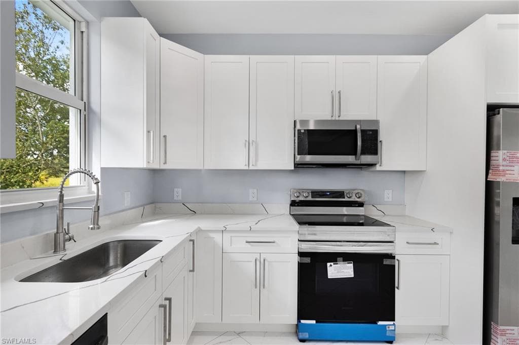 Kitchen with refrigerator, white cabinets, sink, and range with electric stovetop
