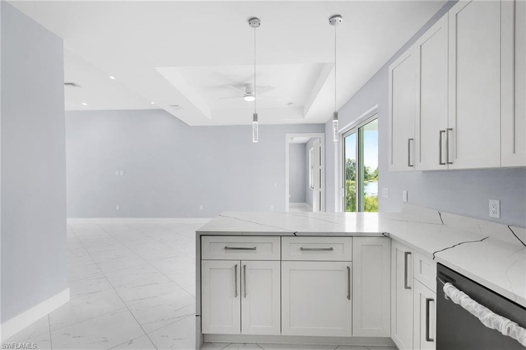 Kitchen featuring light stone countertops, a tray ceiling, white cabinetry, and stainless steel dishwasher