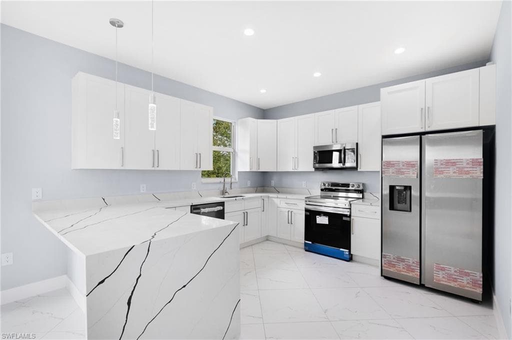 Kitchen featuring hanging light fixtures, light stone countertops, stainless steel appliances, and white cabinets