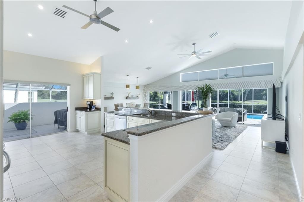 Kitchen with white dishwasher, white cabinetry, pendant lighting, dark stone countertops, and high vaulted ceiling