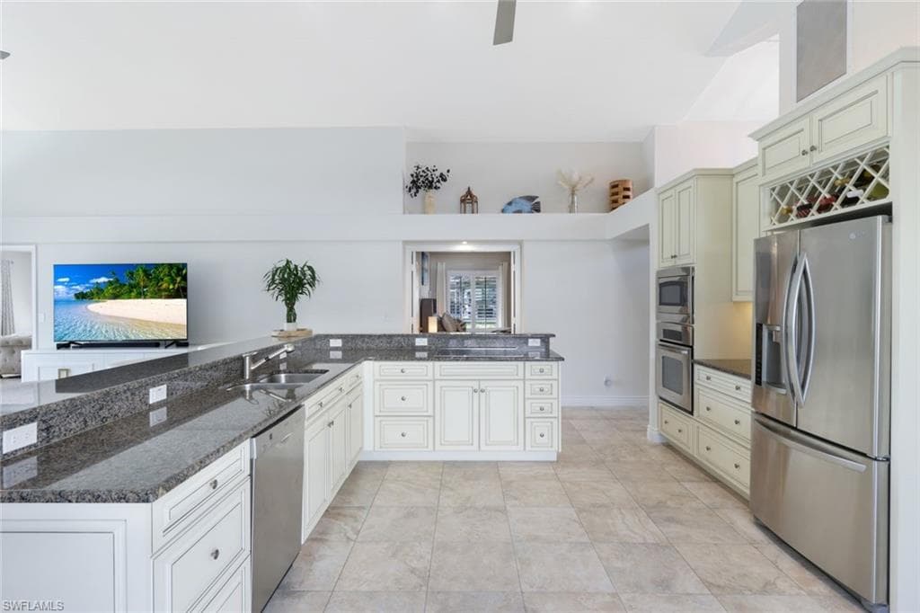 Kitchen with kitchen peninsula, stainless steel appliances, dark stone counters, sink, and light tile patterned flooring