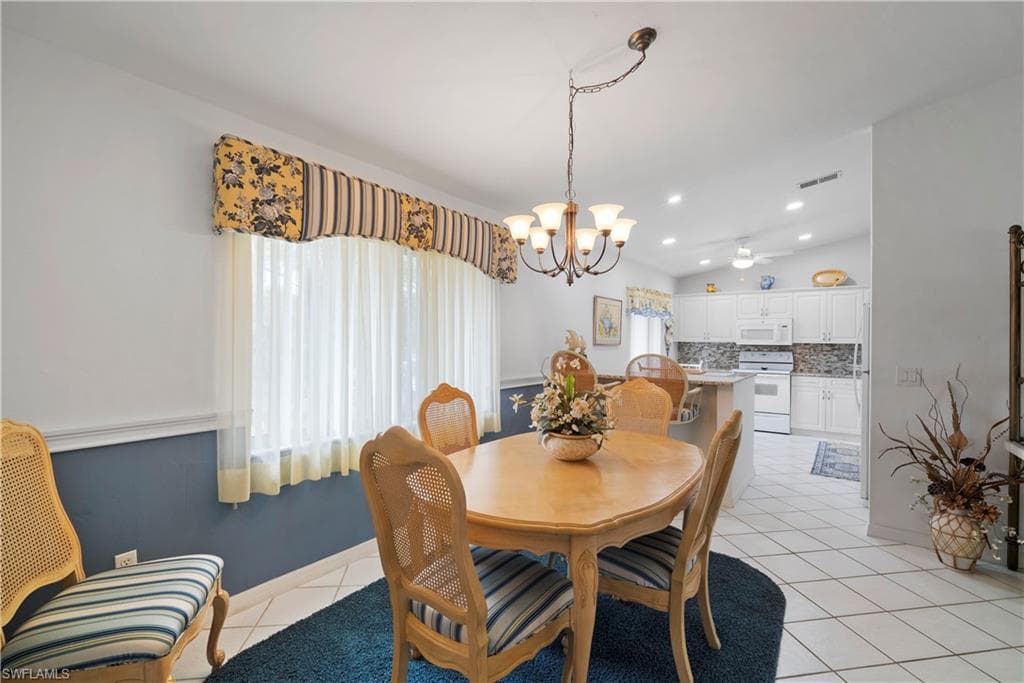 Tiled dining area with lofted ceiling and ceiling fan with notable chandelier