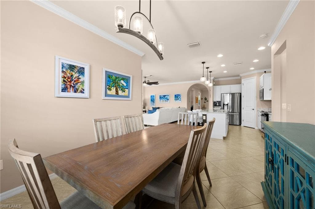 Tiled dining room featuring ceiling fan with notable chandelier and ornamental molding