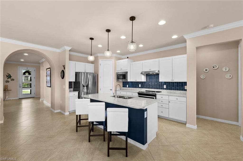 Kitchen featuring ornamental molding, stainless steel appliances, sink, a center island with sink, and white cabinets