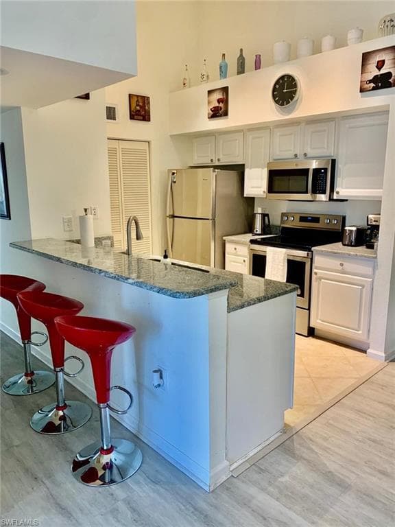 Kitchen featuring appliances with stainless steel finishes, kitchen peninsula, white cabinetry, and sink