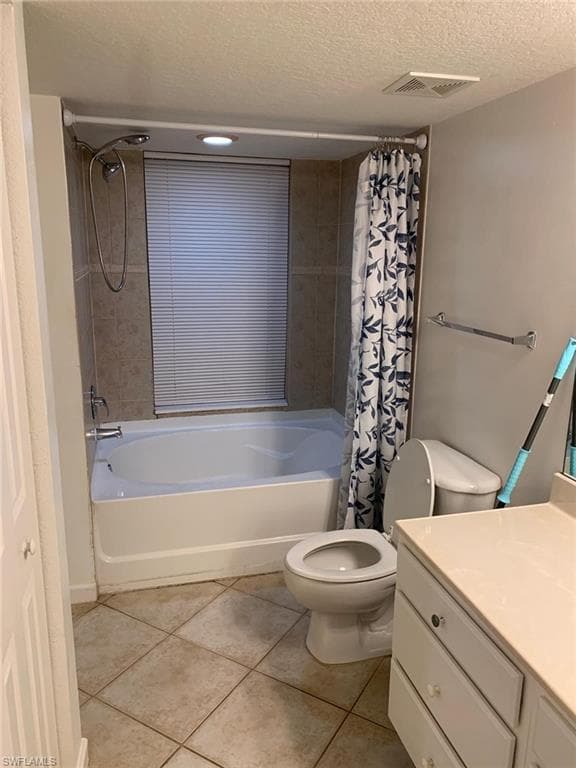 Full bathroom featuring toilet, a textured ceiling, shower / bath combo with shower curtain, and tile patterned flooring