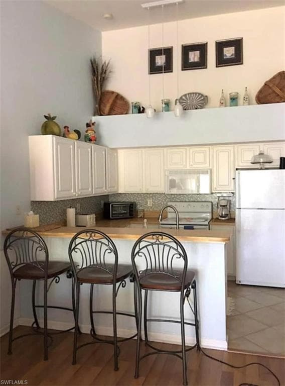 Kitchen with a breakfast bar area, kitchen peninsula, backsplash, and white appliances
