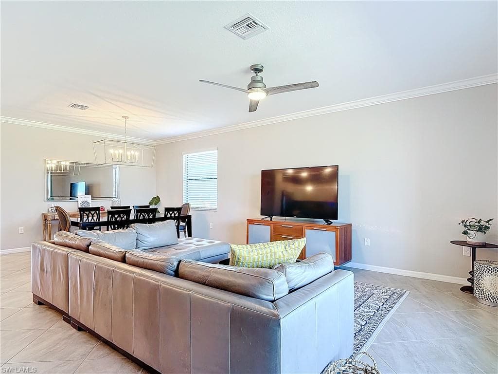 Tiled living room featuring ceiling fan with notable chandelier and crown molding