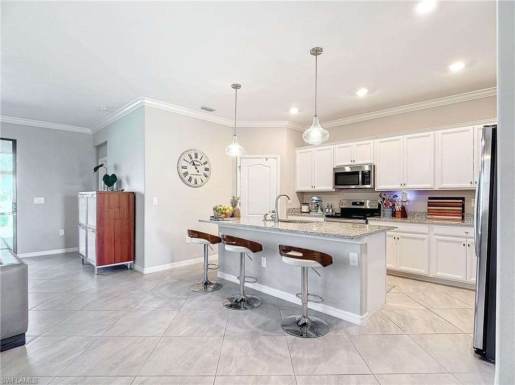 Kitchen featuring white cabinetry, appliances with stainless steel finishes, decorative light fixtures, light stone countertops, and a kitchen island with sink