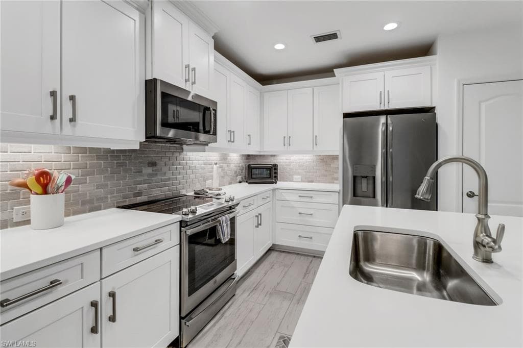 Kitchen with white cabinets, stainless steel appliances, sink, and tile backsplash