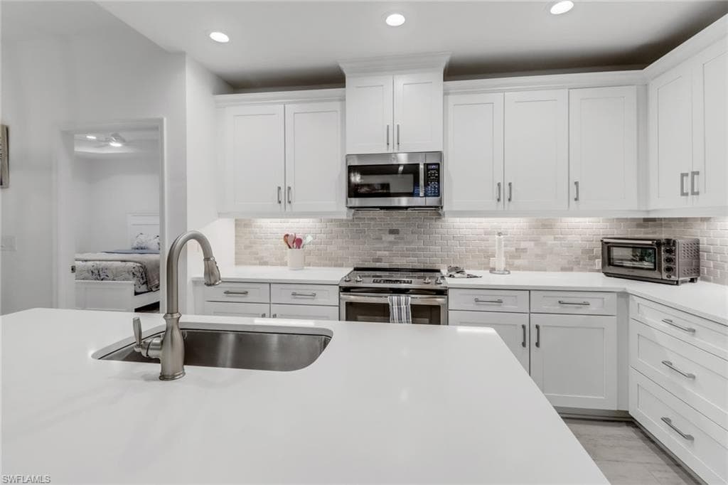 Kitchen with white cabinetry, sink, tile backsplash, and stainless steel appliances