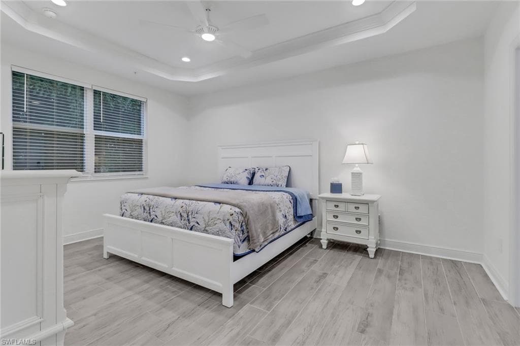 Master bedroom featuring light wood-type flooring, ceiling fan, and a tray ceiling