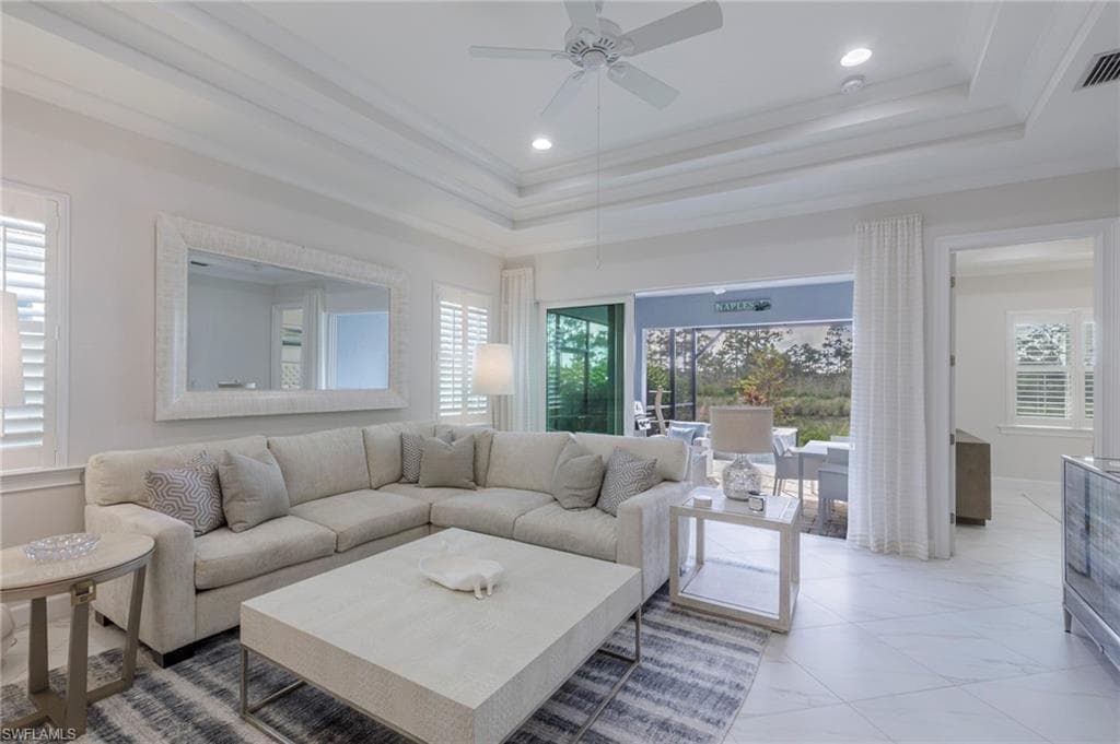 Living room with a raised ceiling, ceiling fan, plenty of natural light, and ornamental molding