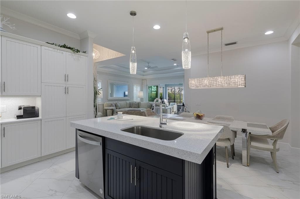Kitchen featuring white cabinets, sink, a center island with sink, dishwasher, and hanging light fixtures