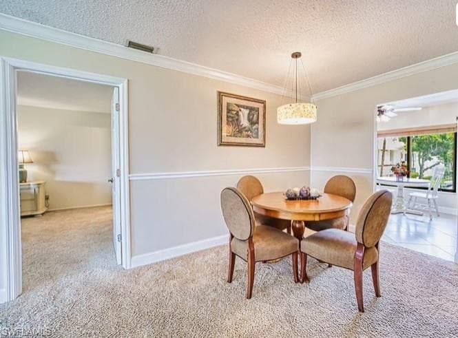 Dining area featuring a textured ceiling, crown molding, ceiling fan, and light carpet