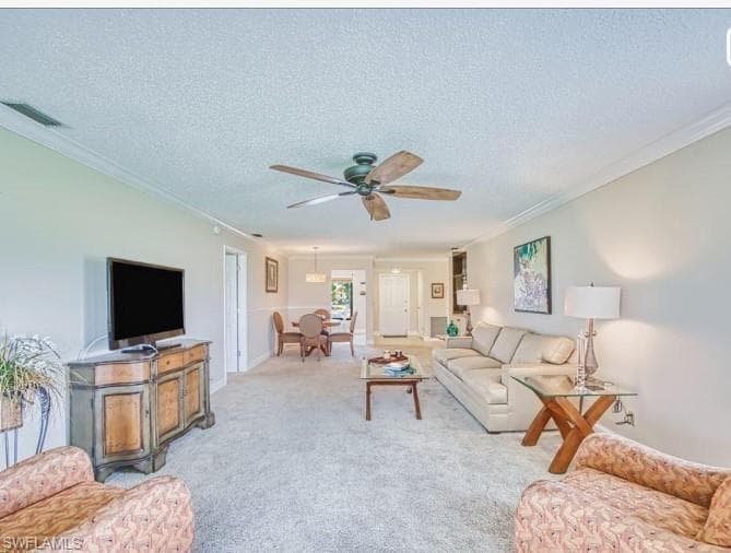 Living room featuring carpet, a textured ceiling, ornamental molding, and a ceiling fan