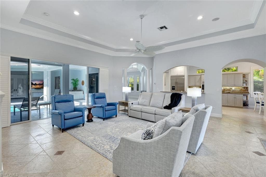 Living room with a tray ceiling, ceiling fan, and crown molding