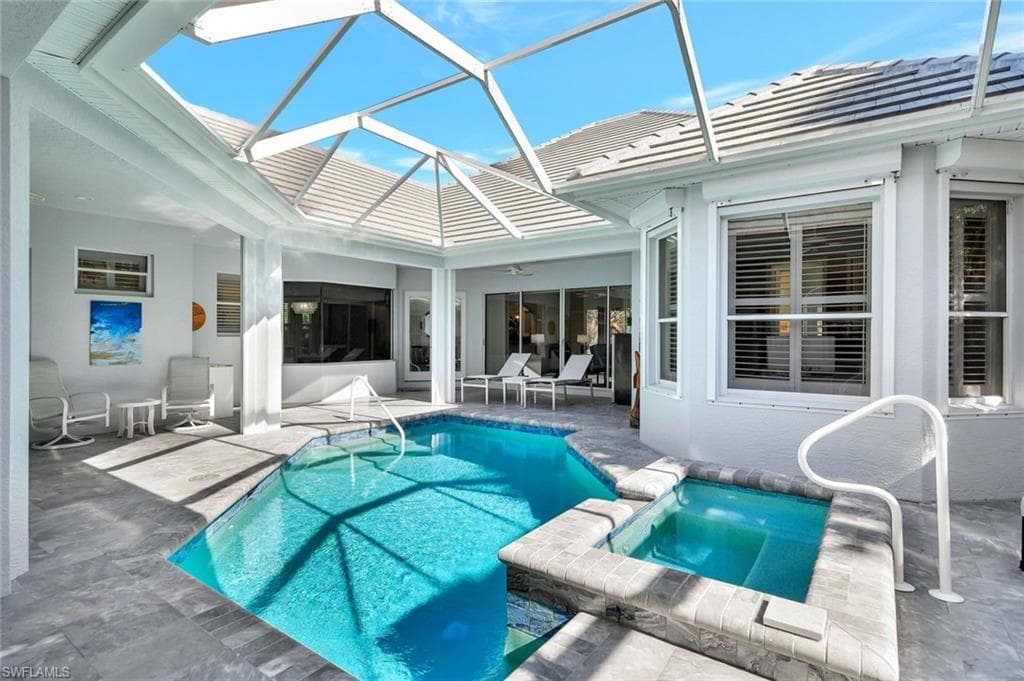 View of pool with glass enclosure, a patio area, and an in ground hot tub