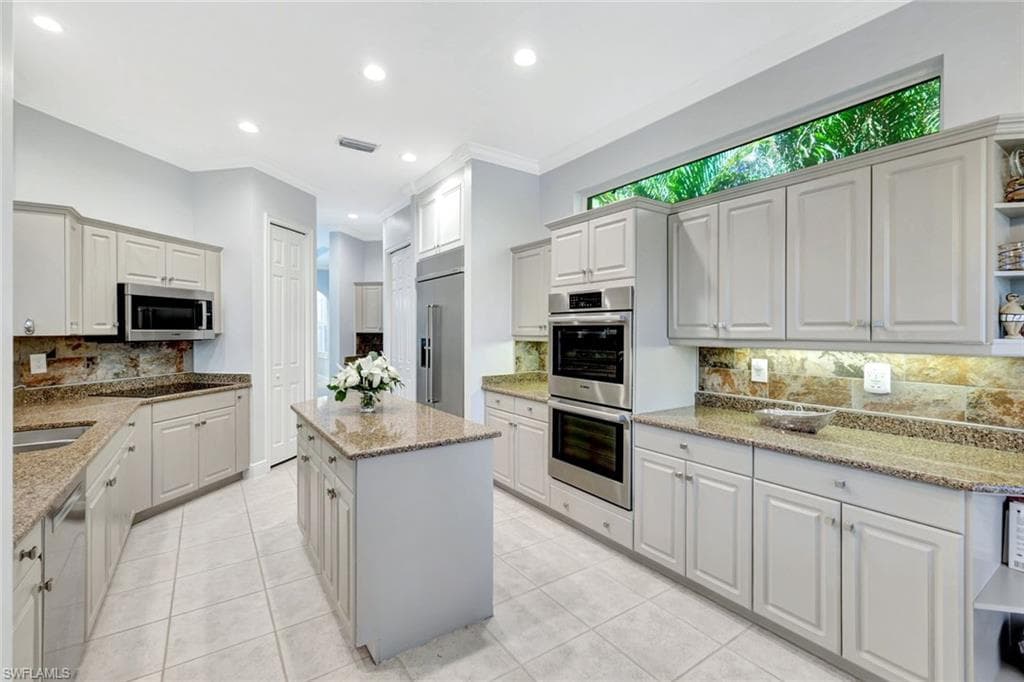 Kitchen with decorative backsplash, appliances with stainless steel finishes, light stone counters, ornamental molding, and white cabinetry