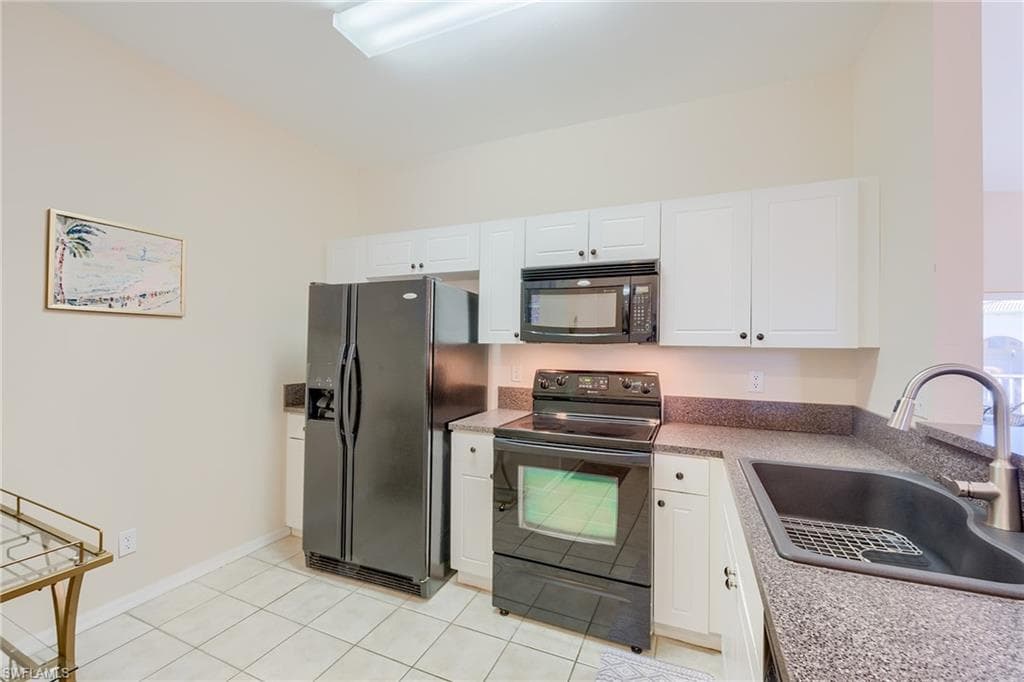 Kitchen featuring black appliances, white cabinets, light tile patterned floors, and sink