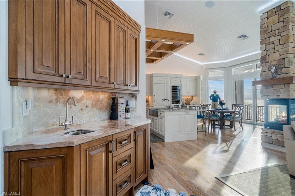 Wet bar featuring sink, a fireplace, light stone countertops, light hardwood / wood-style floors, and backsplash
