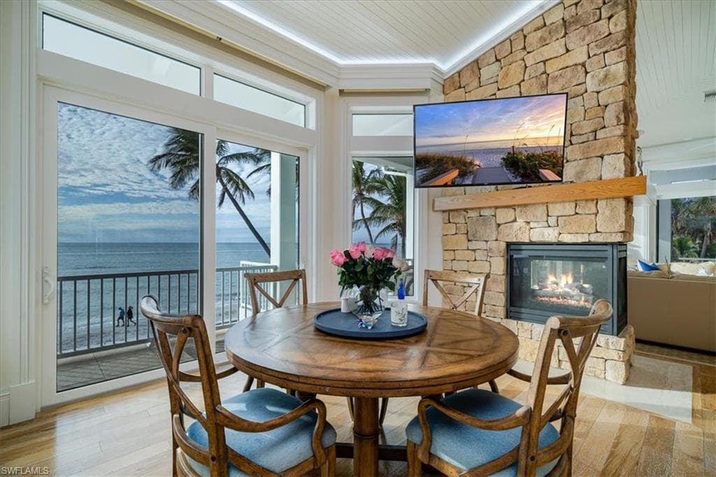 Dining space featuring wood ceiling, a stone fireplace, light hardwood / wood-style flooring, and ornamental molding
