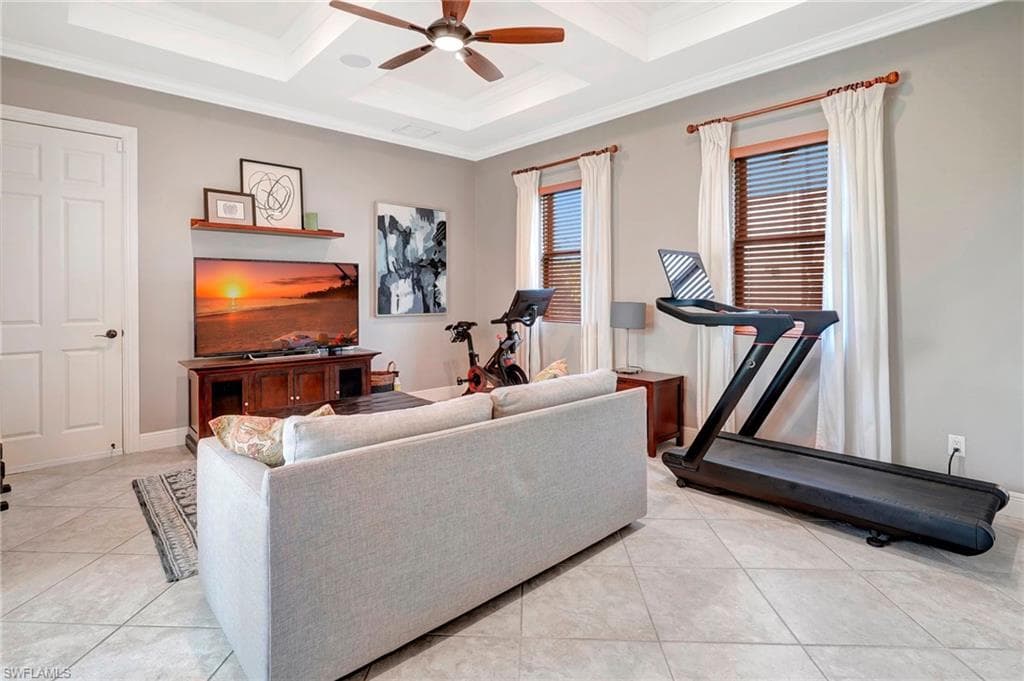 Exercise area with coffered ceiling, light tile patterned floors, ornamental molding, and ceiling fan