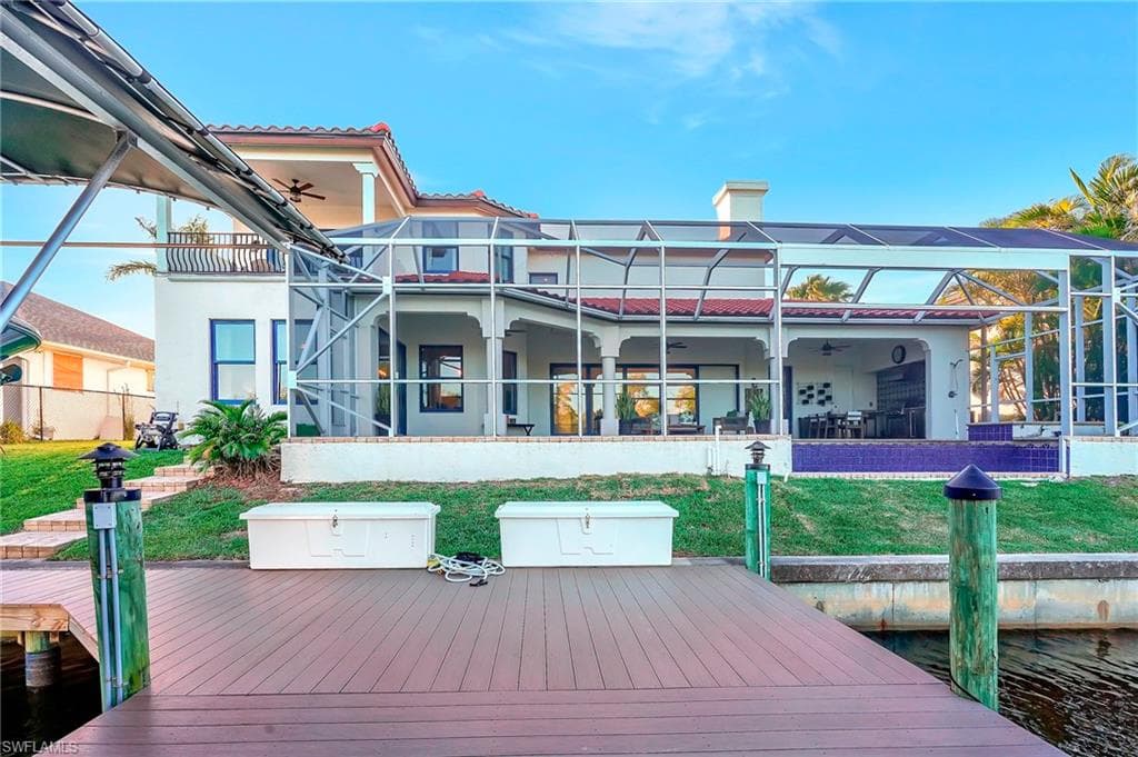 Rear view of house featuring a lawn, a water view, ceiling fan, and glass enclosure