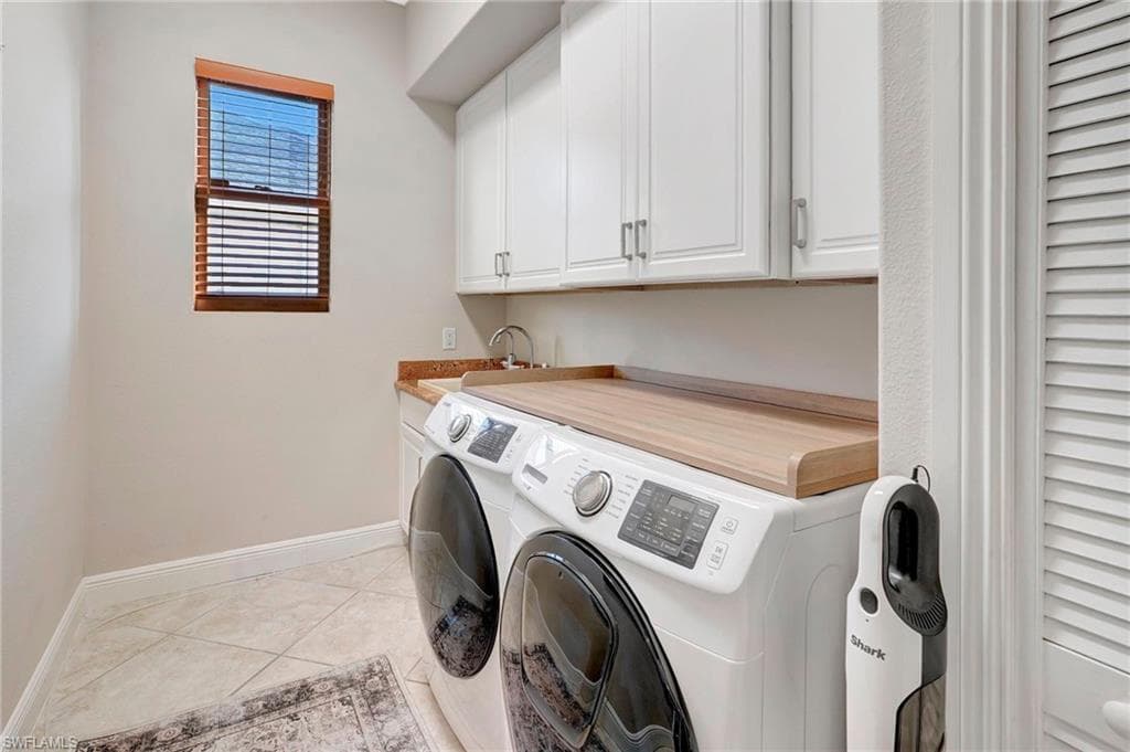 Washroom with cabinets, light tile patterned flooring, washer and dryer, and sink