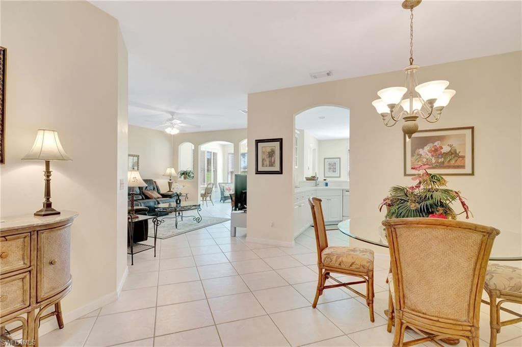 Dining room with light tile patterned floors, ceiling fan with notable chandelier, baseboards, arched walkways, and visible vents