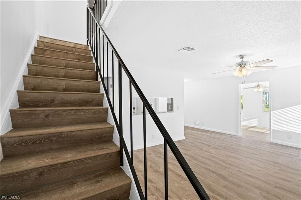 Stairway featuring wood-type flooring, a textured ceiling, and ceiling fan