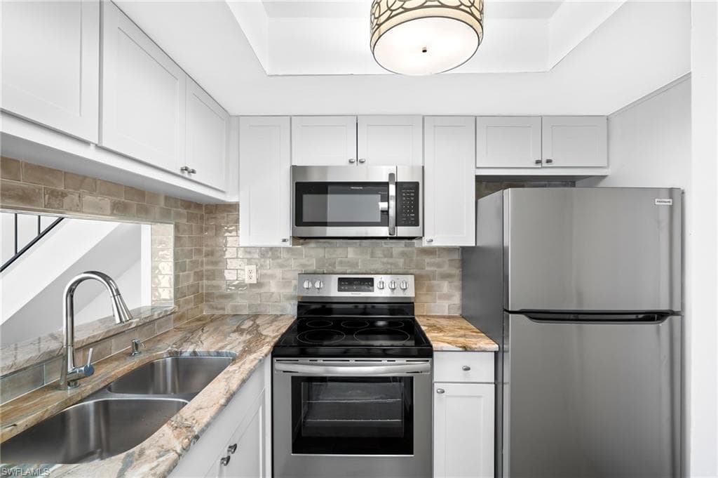 Kitchen featuring light stone counters, white cabinetry, sink, and appliances with stainless steel finishes