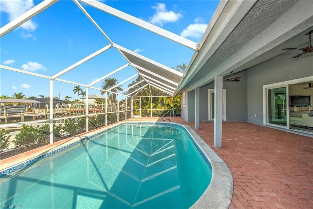 View of pool with ceiling fan, a lanai, a water view, and a patio area