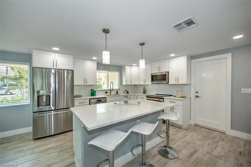 Kitchen featuring stainless steel appliances, sink, white cabinetry, a center island, and pendant lighting
