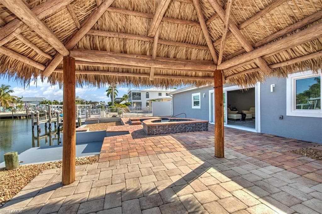 View of patio / terrace with a gazebo, a boat dock, an in ground hot tub, and a water view