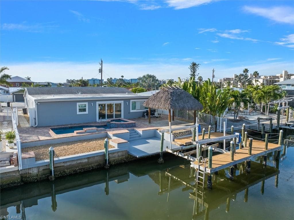 View of dock with a water view, a swimming pool with hot tub, and a patio
