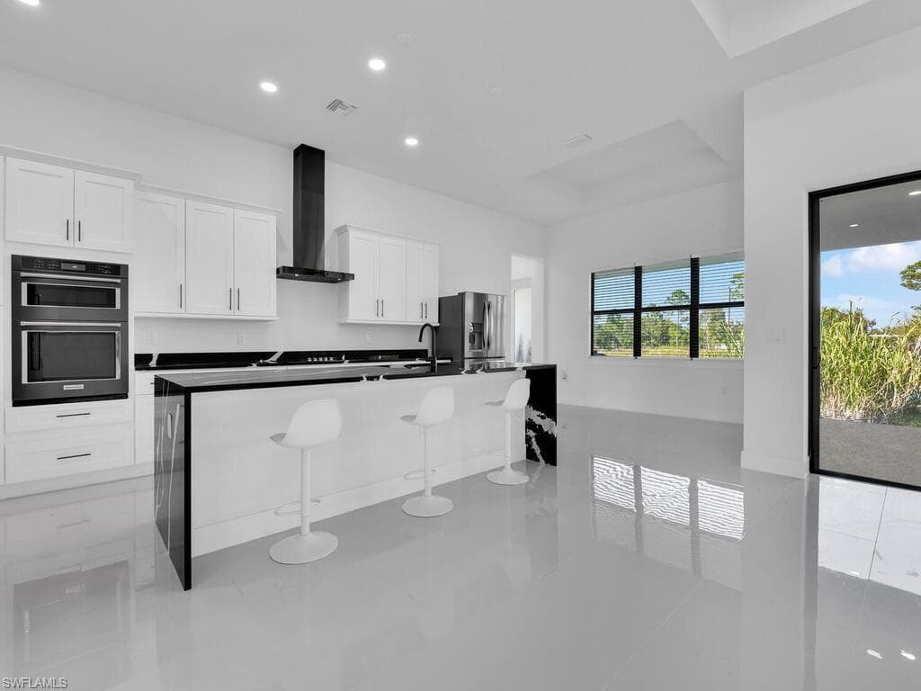 Kitchen with a center island with sink, stainless steel fridge with ice dispenser, a kitchen breakfast bar, white cabinets, and wall chimney exhaust hood