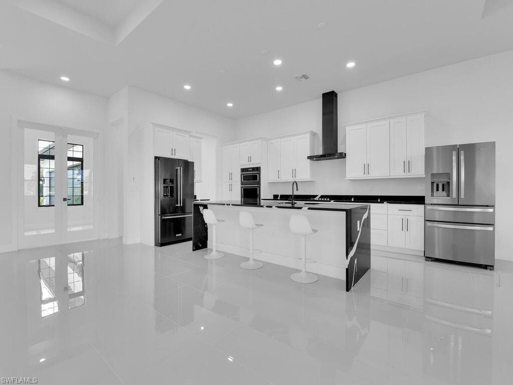 Kitchen with wall chimney range hood, stainless steel refrigerator with ice dispenser, high quality fridge, white cabinetry, and an island with sink