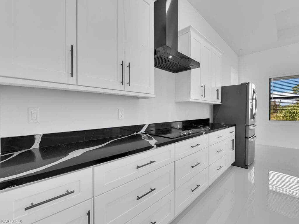 Kitchen featuring white cabinets, stainless steel fridge, wall chimney range hood, and black electric stovetop