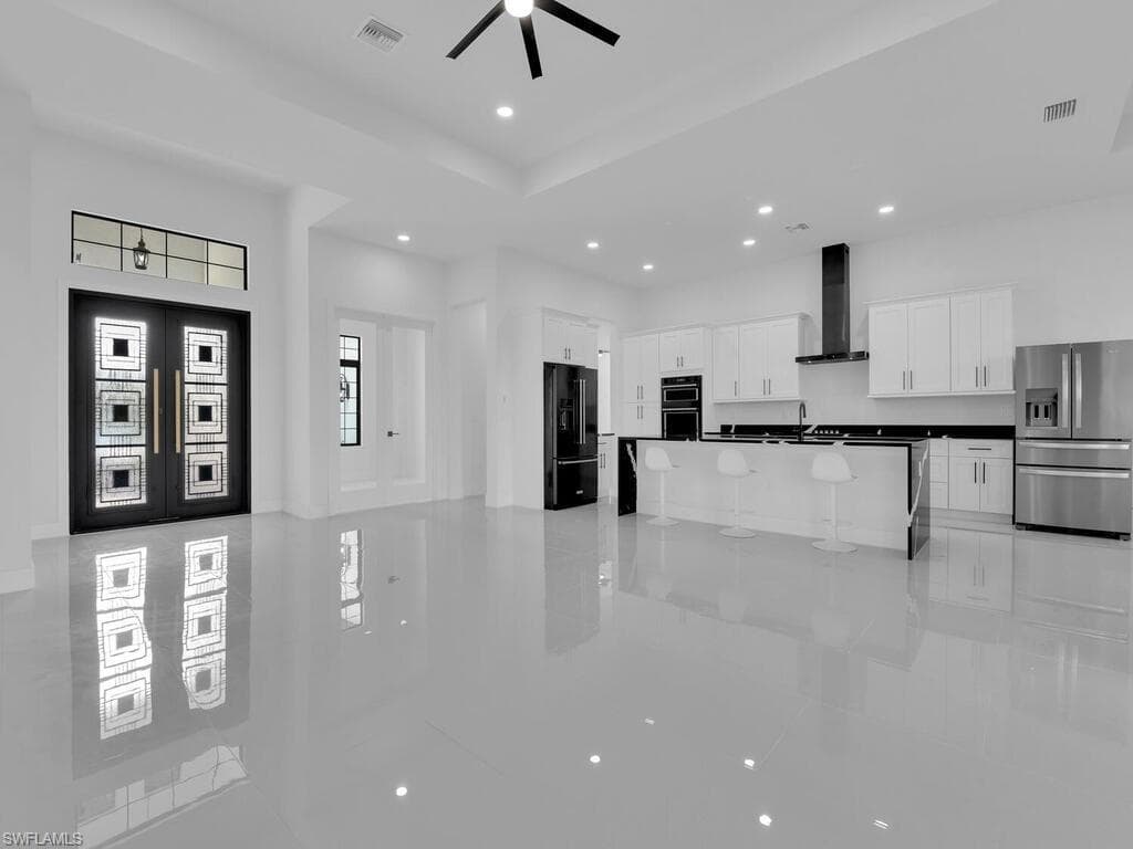 Kitchen with white cabinetry, ceiling fan, wall chimney range hood, black appliances, and a center island