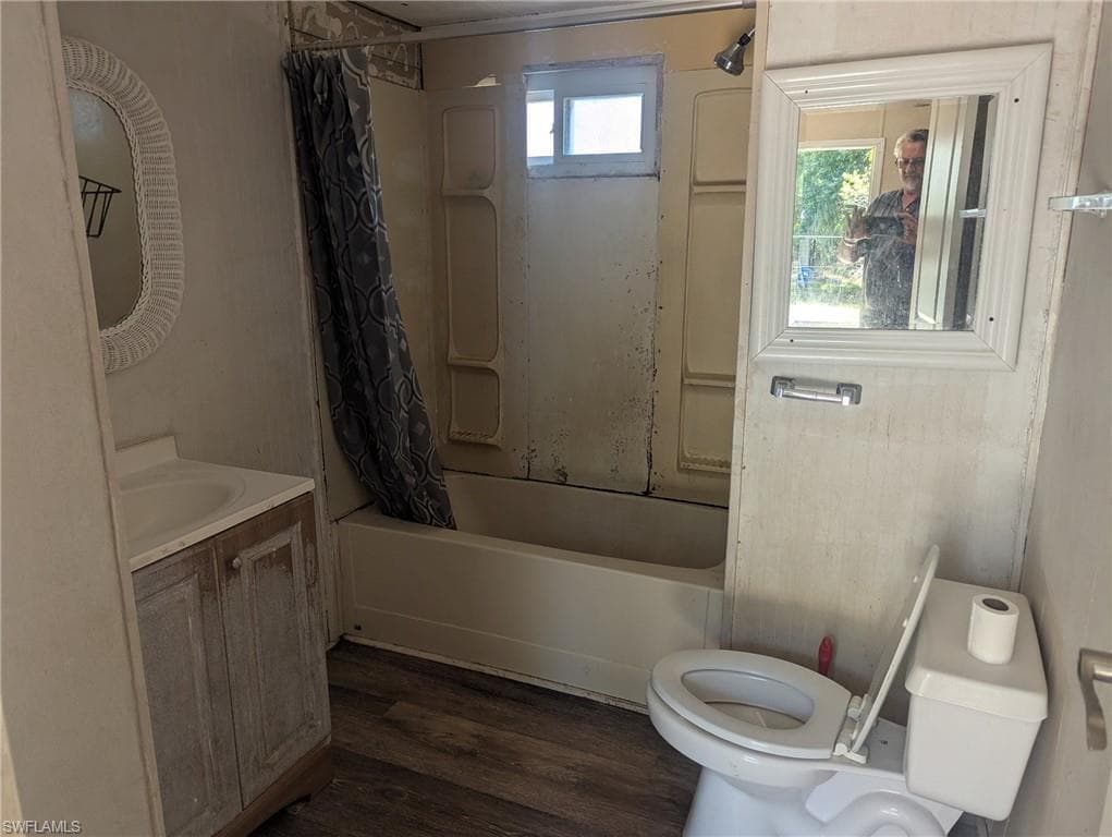 Bathroom with toilet, shower / bathtub combination with curtain, vanity, and wood finished floors