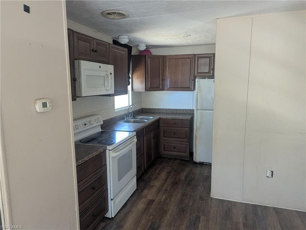 Kitchen featuring visible vents, a sink, dark wood-style flooring, white appliances, and dark brown cabinets