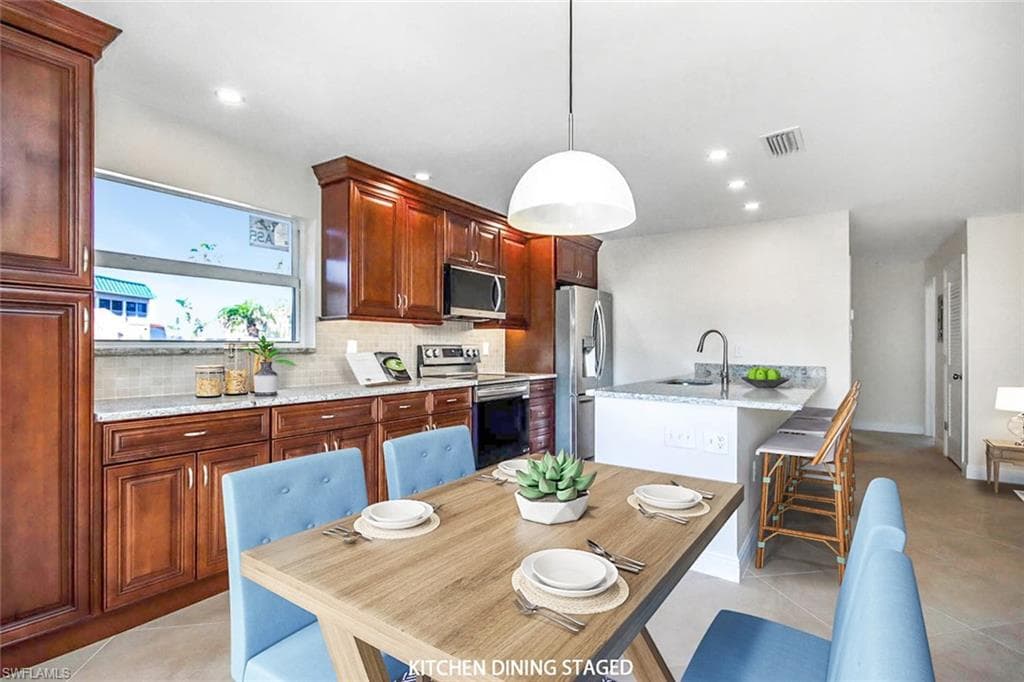 Kitchen featuring light tile patterned floors, stainless steel appliances, tasteful backsplash, hanging light fixtures, and a breakfast bar