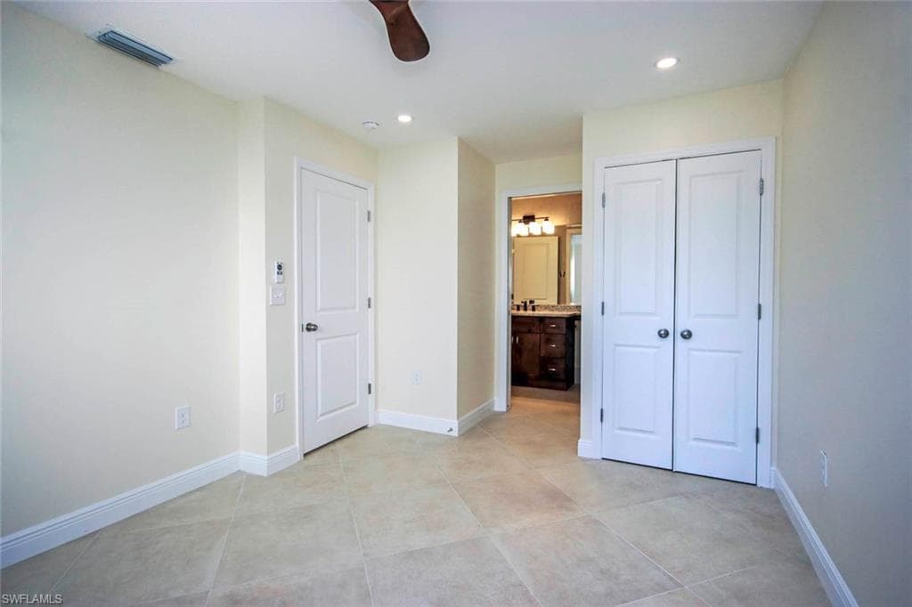Unfurnished bedroom with ceiling fan, light tile patterned floors, a closet, and ensuite bath